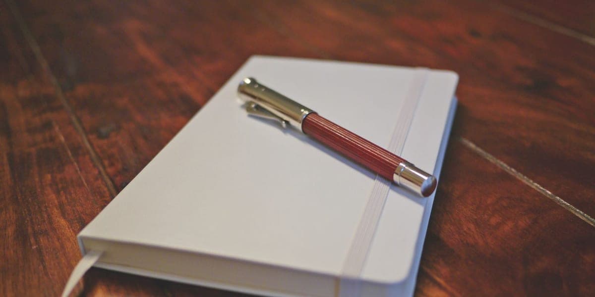 A brown pen resting on a closed white notebook on a wooden table