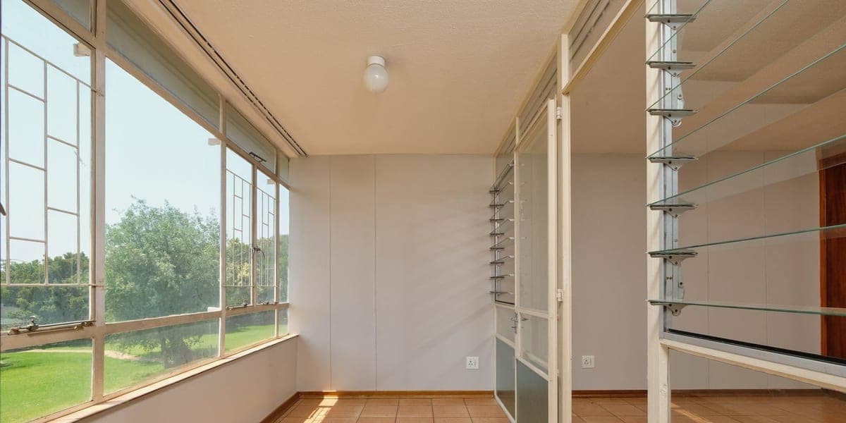 Sunlit empty room with large windows overlooking green trees