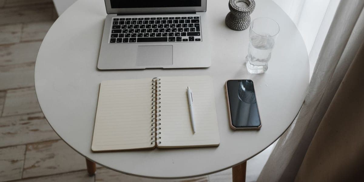 Open notebook and pen beside a laptop and phone on a round table